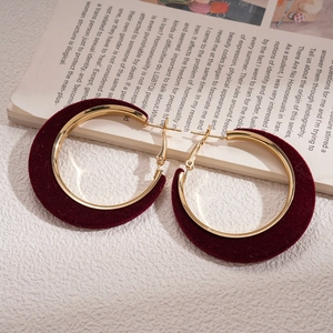 Detailed close-up of wine red velvet wrapped gold hoop earrings on a textured paper