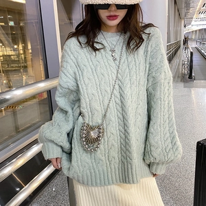 Women's light green cable knit sweater styled with silver heart-shaped crossbody bag