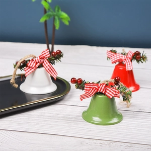 Three metal Christmas bells in white, green, and red with pine branch and ribbon bows