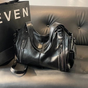 Vintage black faux leather tote bag with stud details and detachable strap on leather sofa