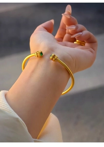 Detailed close-up of 24k gold plated open bangle with green zircon and hollow carving