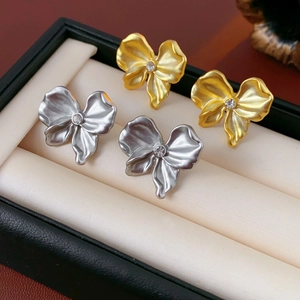 Detail of silver and gold pleated bow earrings with sparkling central zircon stones