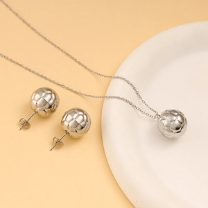 Detail shot of silver soccer ball necklace and stud earrings set on a minimal display