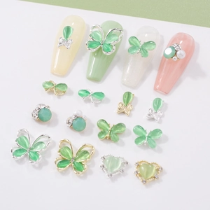 Macro detail of green cat-eye stone butterfly and heart nail art charms on nail tips