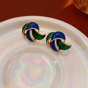 Macro detail of vintage gold stud earrings with blue and green enamel on a holographic tray