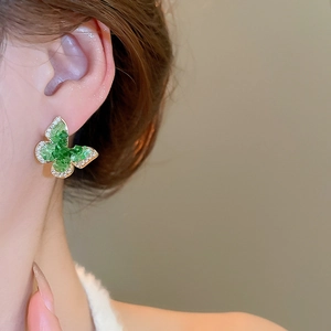 Detailed macro view of 18k gold butterfly earrings with emerald crystals and zircon accents