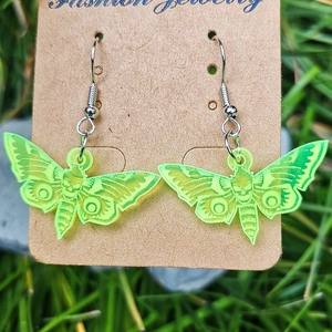 Detailed macro shot of fluorescent green skull moth earrings displayed on grass background