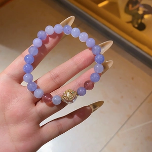 Detailed shot of purple beaded bracelet with gold hollow charm held in hand
