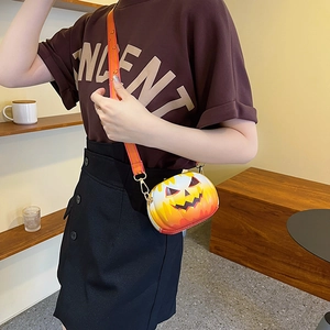 Detail of a round orange pumpkin jack-o'-lantern crossbody bag with a wide patterned strap
