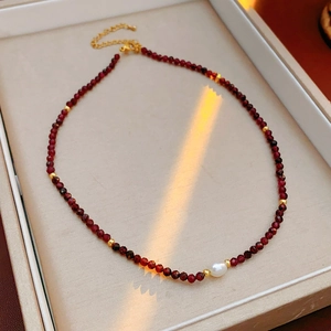 Detailed macro view of dark red garnet beads necklace with white freshwater pearl and gold clasp