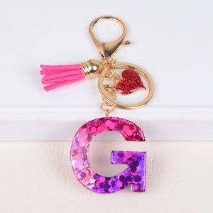 Detail of pink tassel and resin letter G keychain with sparkly glitter and heart charm