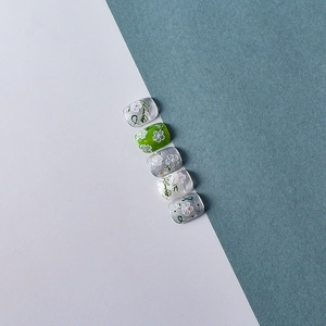 Detail of short round nail tips with white daisies, vine patterns, and silver glitter accents