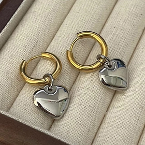 Détail macro de boucles d'oreilles cœur bicolores avec créoles dorées et pendentifs polis