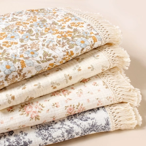 Detailed stack of printed cotton baby blankets with decorative fringe edges and floral patterns