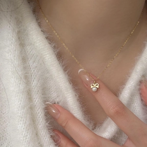 Detail of a gold bow necklace with white pearl pendant worn on a soft white sweater