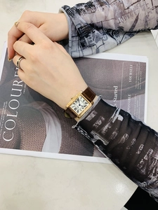 Elegant rectangular gold watch with white Roman dial and brown leather strap on a magazine