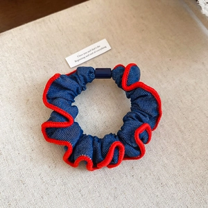 Macro detail of navy denim scrunchie with white polka dots and red wavy stitching edges