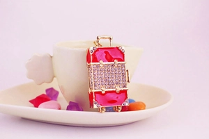 Close-up of red rhinestone suitcase keychain charm in a decorative white cup