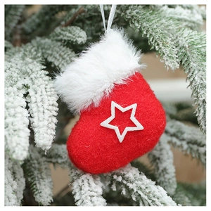 Detail of red plush Christmas sock ornament with white star hanging on snowy pine tree