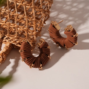 Detail of brown faux leather U-shaped earrings with golden bead accents and steel needle