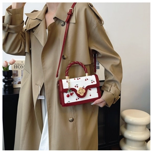 Detail of cherry print handbag with golden flower clasp and woven red handle on model