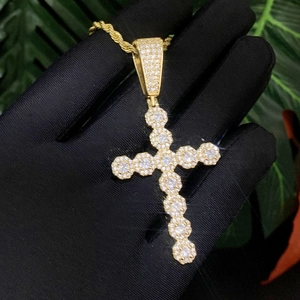 Macro shot of gold cross pendant with cubic zirconia stones held by a gloved hand