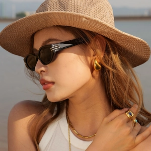 Close-up of golden teardrop earrings and a gold ring with blue gemstone in the sun