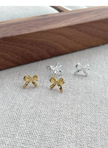 Detailed comparison of gold and silver bow stud earrings on a beige linen background
