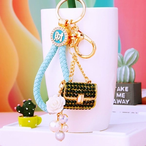 Detail of keychain featuring green rhinestone mini bag and blue woven leather strap