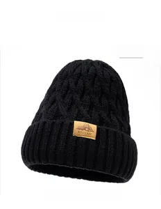 Close-up of black cable knit beanie with brown leather logo patch and warm winter texture
