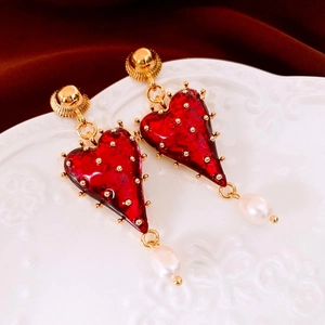 Macro view of vintage heart pearl drop earring with gold details on red velvet