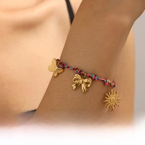 Vue macro d'un bracelet tissé coloré avec des breloques papillon et soleil dorées