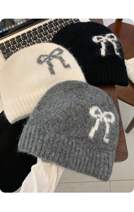 Three mohair knit beanies in black white and grey with bow patterns on a desk