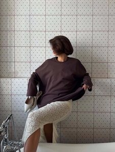 Oversized dark brown sweater and white lace skirt outfit shown in lifestyle shot