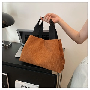 Détail de sac à main en velours côtelé marron avec poignées noires dans un décor élégant.
