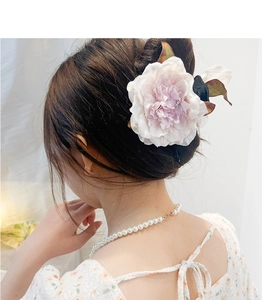 Rear view of a model wearing a pink and white gradient rose hair claw with green leaves