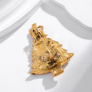 Golden Christmas tree brooch with back safety pin fastener on a minimalist stone background