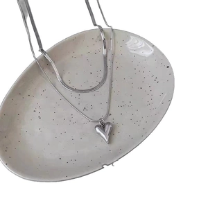Double-layered silver heart pendant necklace with flat snake chain on white ceramic plate