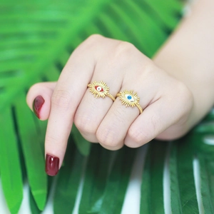 Detail of gold evil eye rings with red and blue accents on a green leaf background