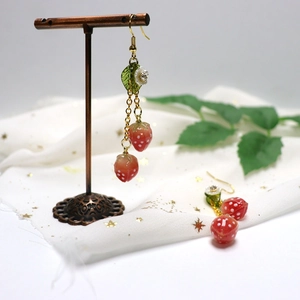 Detail of strawberry drop earrings with green leaves and white flowers on gold hooks