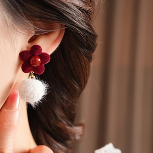 Detailed close-up of a burgundy velvet flower earring with a white fluffy pompom on a model