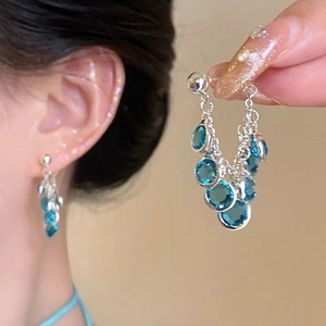 Close-up of elegant silver tassel earrings with blue round gems on model and in hand