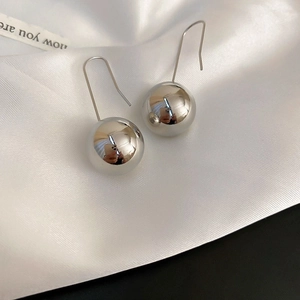 Close-up of polished silver ball drop earrings on white silk fabric background