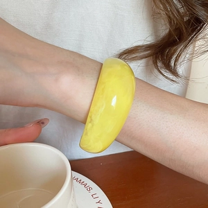 Macro shot of a minimalist wide yellow resin bangle with inner cloudy textures on a model's wrist