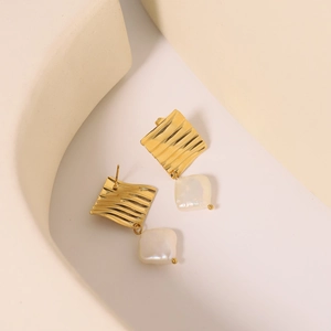 Baroque pearl earrings with golden wavy square plates on a minimalist creamy background