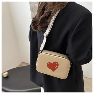Detail of beige crossbody camera bag with red heart print and wide textile strap