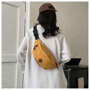 Detail of yellow canvas chest bag with adjustable strap and leather logo on white hoodie