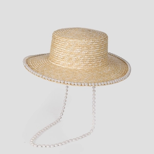 Detailed view of beige straw boater hat with white pearl trim and elegant pearl chain strap