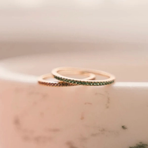 Close-up of rose gold eternity rings with micro-pave green and brown gemstones