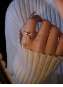 Close-up of gold bow ring with sparkling zircons and elegant hanging white pearls